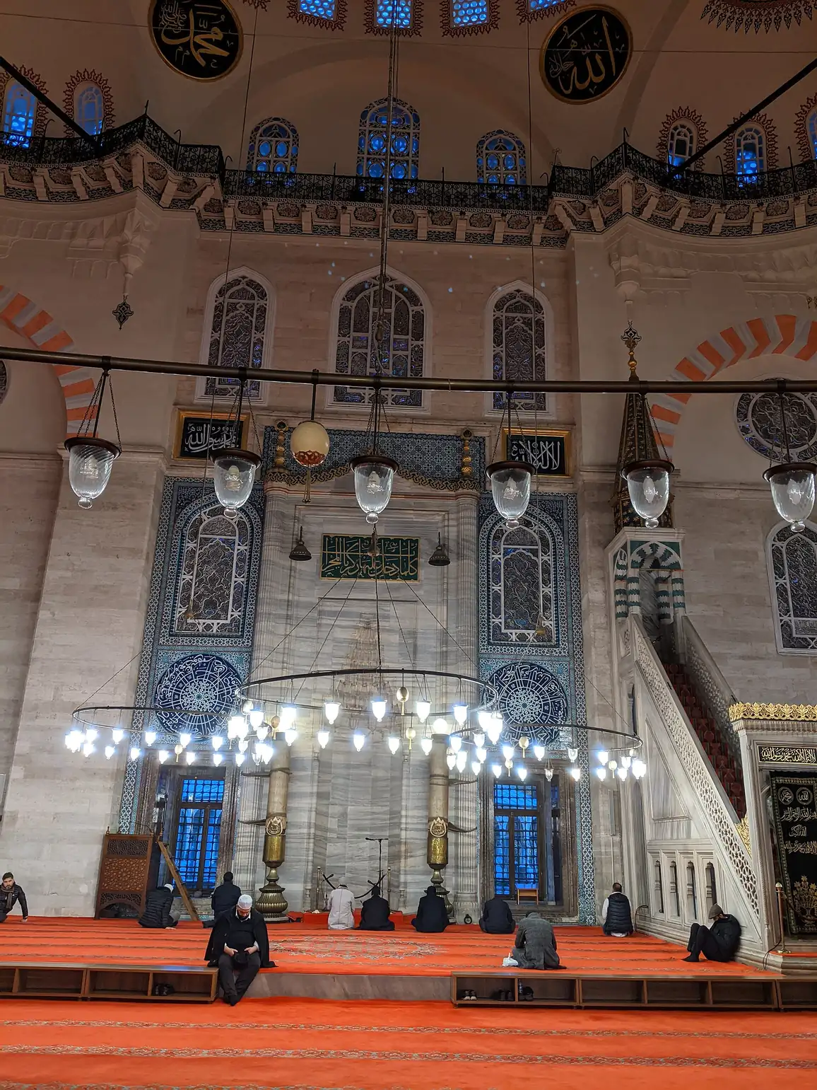 Glass lamps hanging in the Süleymaniye Mosque prayer hall as worshippers wait for Maghrib.